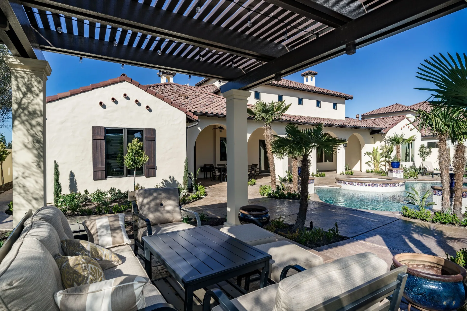 Custom-home courtyard with a swimming pool, covered outdoor seating, arched patios, and palm landscaping.