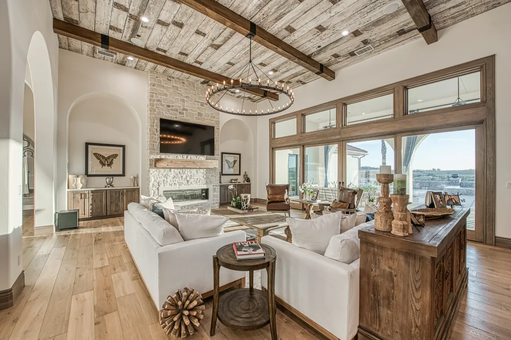 Custom living room at Friant Estate featuring a stone fireplace, reclaimed-wood ceiling, exposed beams, and expansive windows.