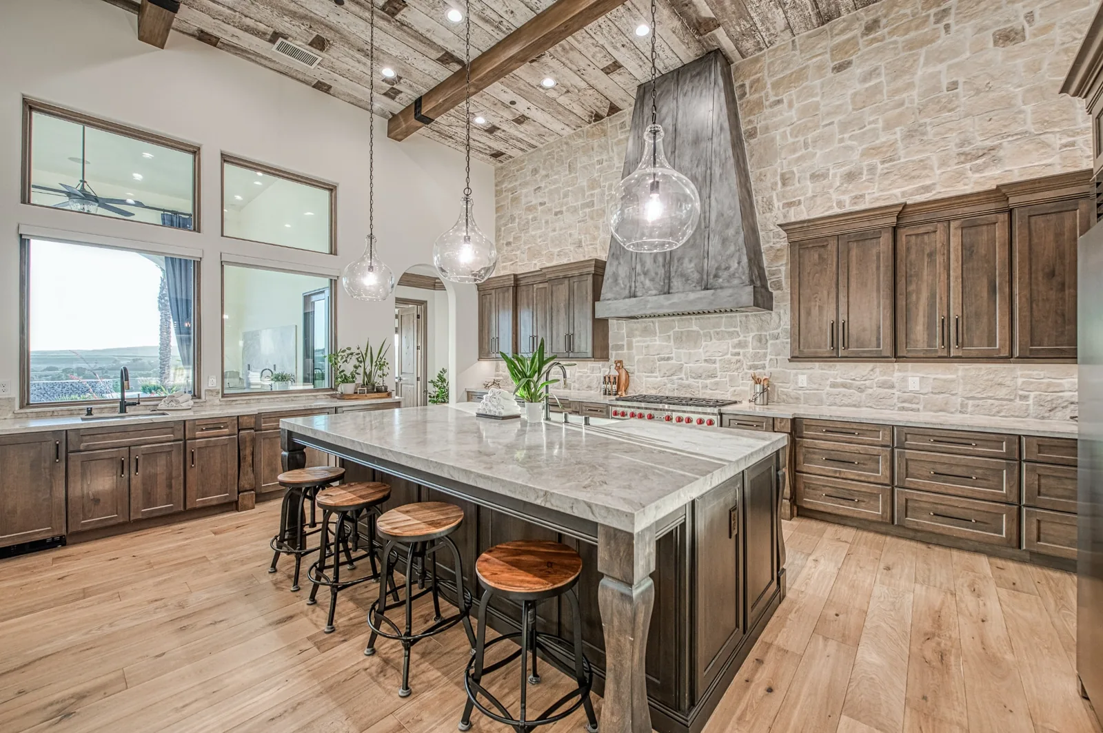 Custom luxury kitchen with a stone feature wall, wood-beamed ceiling, and oversized island.