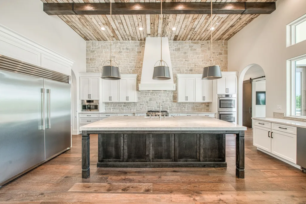 Symmetrical kitchen view with a plaster hood, stone backsplash, and dark island at Ashlan Estate.