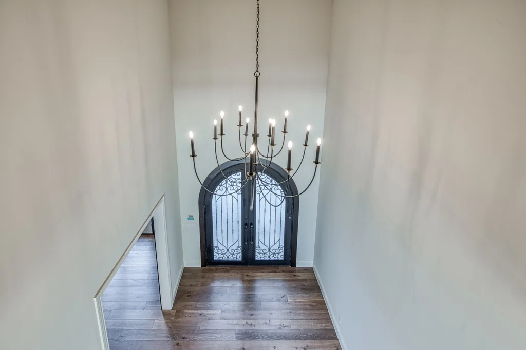 Two-story entry foyer with arched iron and glass doors beneath a tiered iron chandelier.