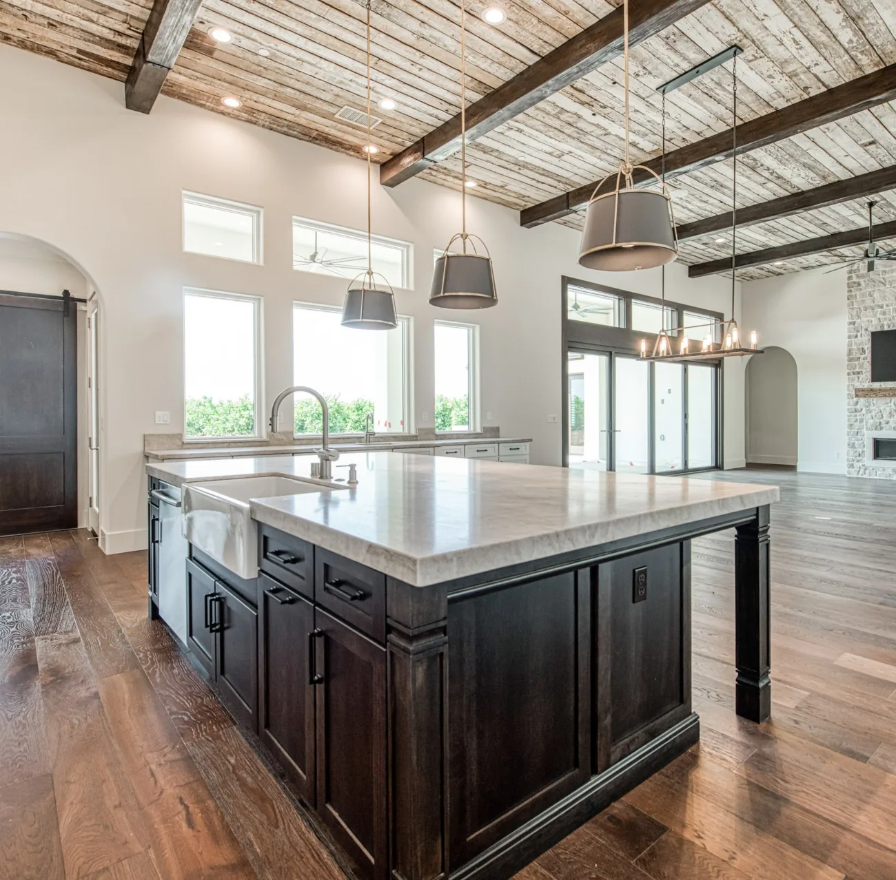 Custom home great room and kitchen with reclaimed wood beam ceiling, marble island, and sliding barn door, showcasing the craftsmanship of Legacy Custom Homes.